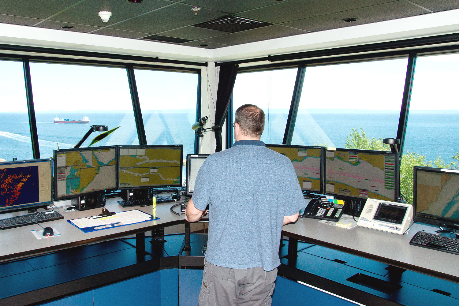 Photo of a man in front of several computer screens and watching a vessel through the window
