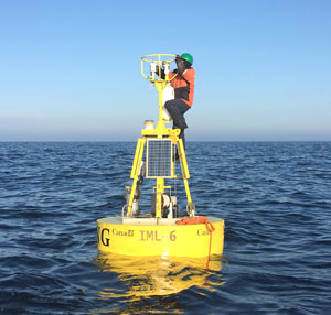 A man kneeling, performs maintenance on a scientific buoy