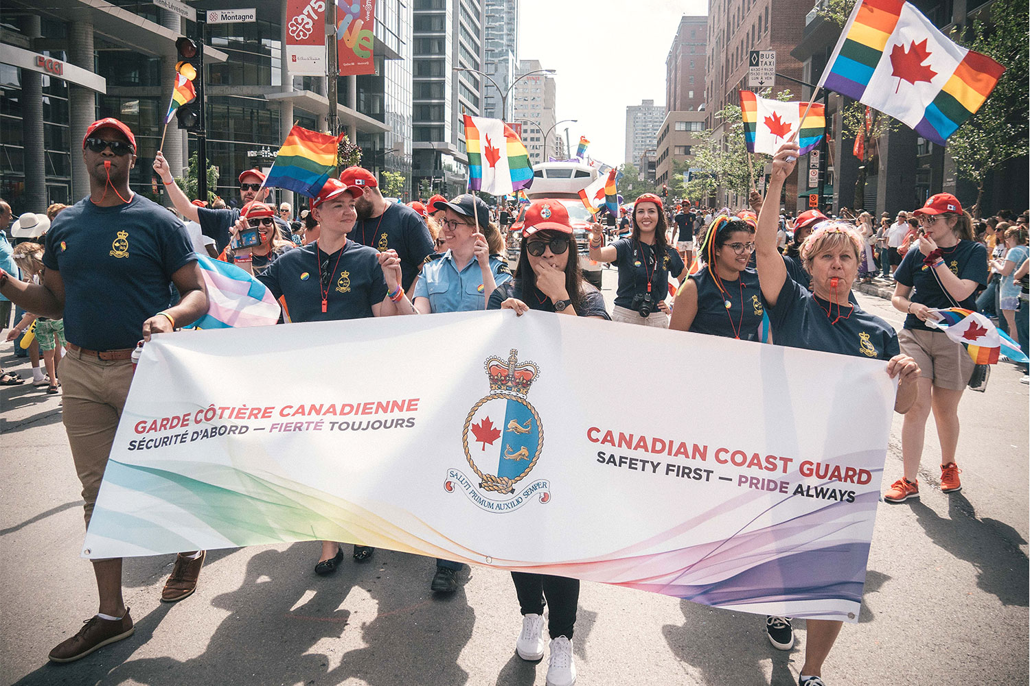 Photo of Canadian Coast Guard members sporting flags and a banner, parading through the streets of Montreal
