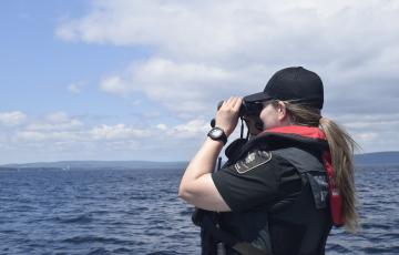 Une agente des pêches regarde au loin avec des jumelles